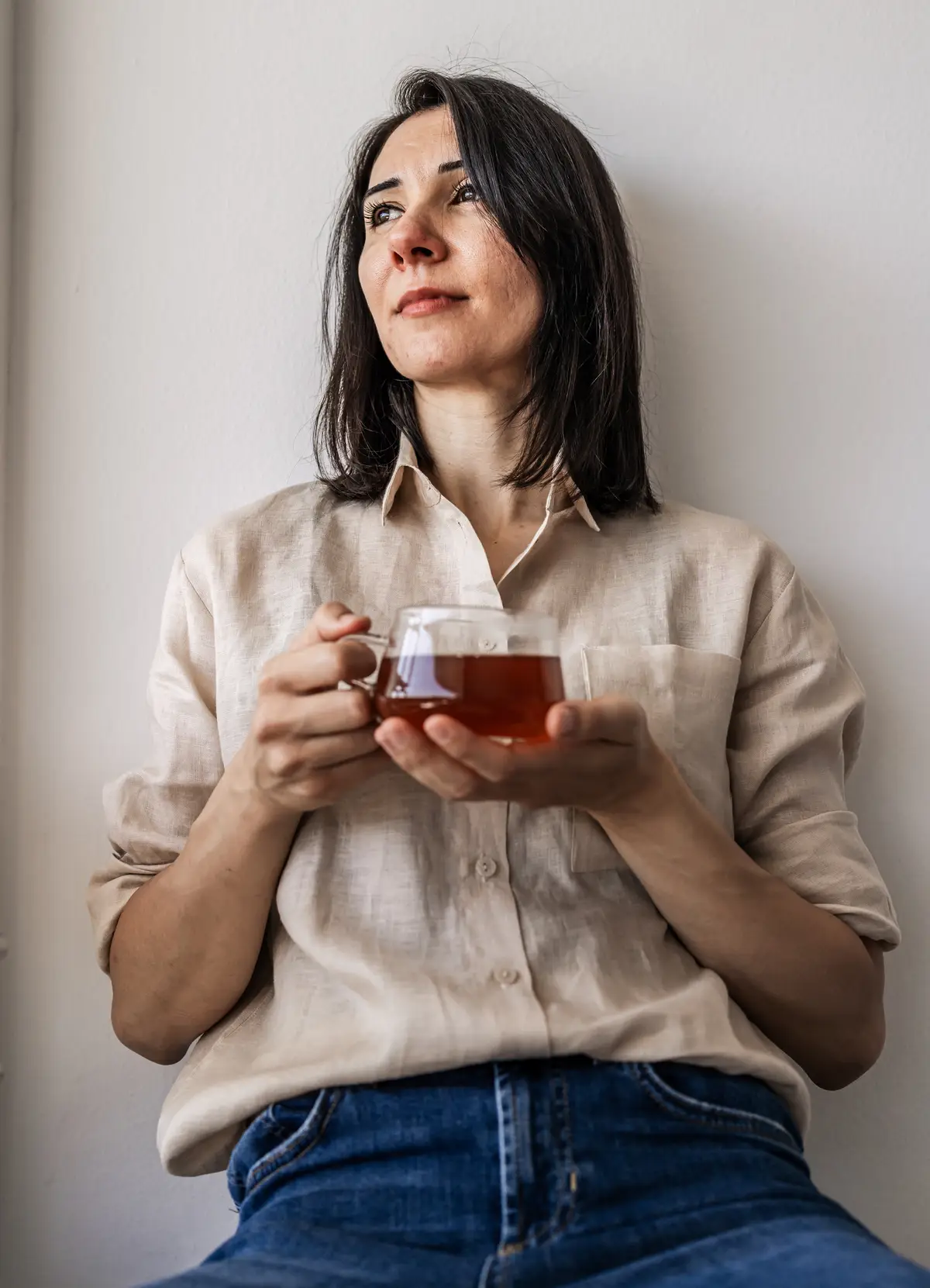 Entspannte Frau hält eine gläserne Tasse mit dampfendem Tee in den Händen