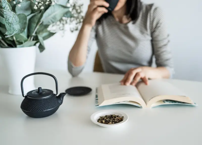 Donna che si gode una tazza di tè leggendo un libro in un angolo luminoso