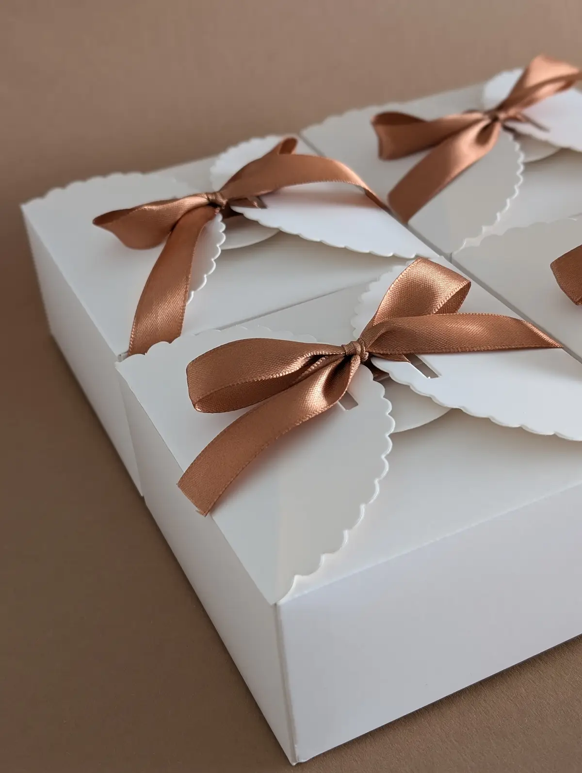 Scatole regalo bianche per bomboniere decorate con fiocchi in raso color bronzo su fondo neutro