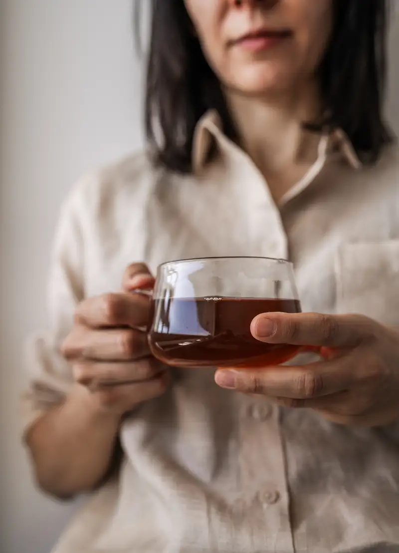 Close-up of a transparent glass cup filled with amber tea infusion held in hands