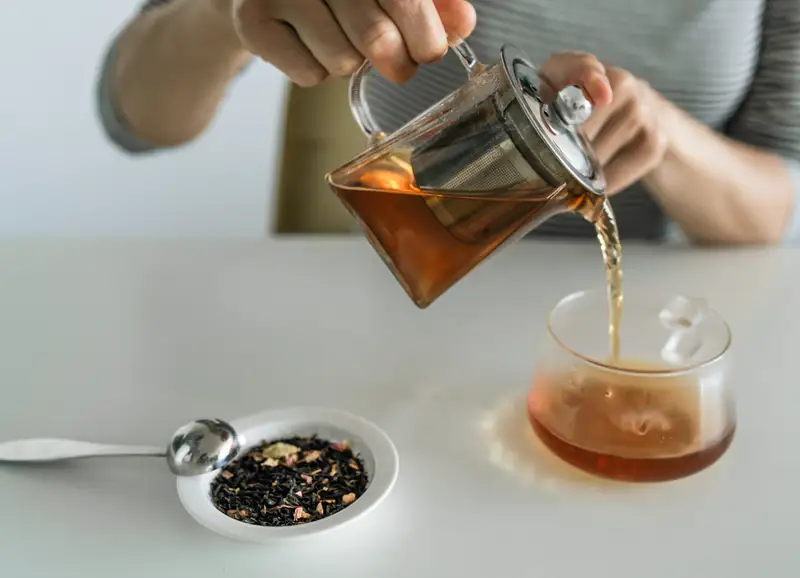 Hands pouring tea into a cup from a glass teapot
