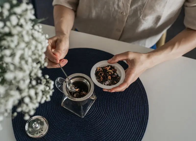 Hands preparing tea by placing loose leaves into the infuser
