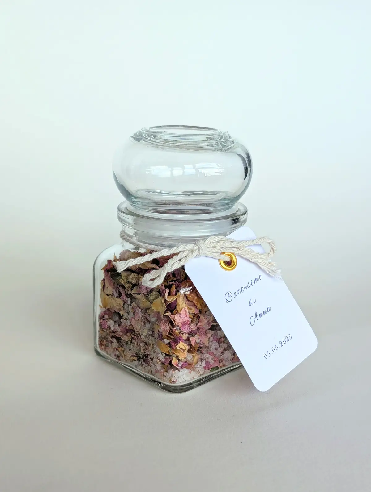 Close-up of a glass wedding favour jar filled with flower petals and cooking salt, custom tag, and satin ribbon